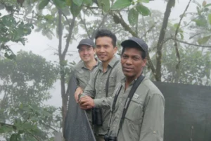 Three Mashpi Lodge guides in the misty cloud forest, one holding binoculars, ready for a day of exploration.