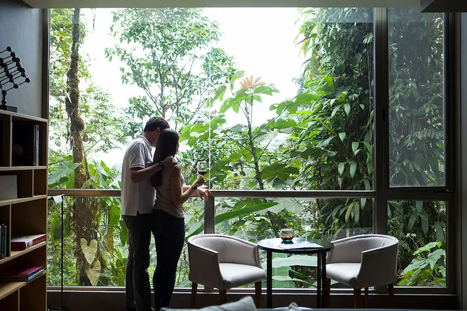A couple shares an intimate moment while gazing into the lush cloud forest from the expansive windows of Mashpi Lodge in Ecuador.
