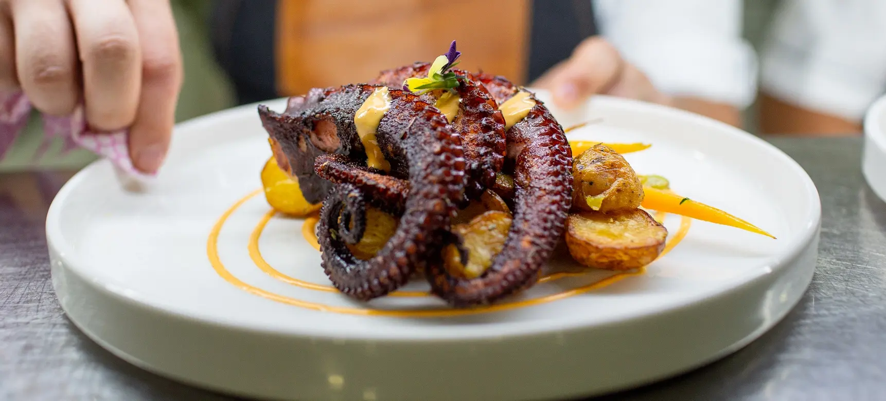 mashpi lodge cuisine superb dining Grilled octopus over roasted potatoes with a spicy aioli drizzle on a white plate, showcasing Mashpi Lodge's culinary delights.